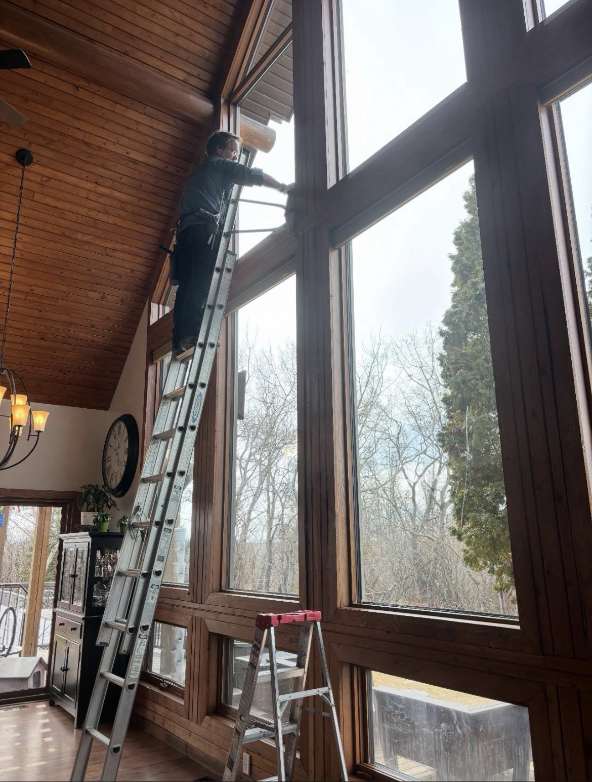 Ryan on a ladder cleaning a tall cathedral window from the inside